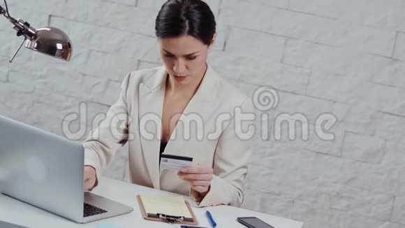 年轻漂亮的女商人用信用卡打电话视频的预览图