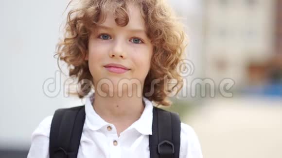 普雷特恩卷曲的蓝眼睛男孩笑着看着相机男生穿着白衬衫背着一件视频的预览图