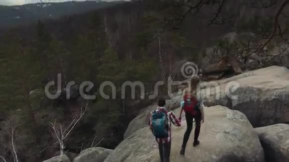 鸟瞰可爱的夫妇与时尚的背包牵着手和走在岩石阿尔卑斯山危险的悬崖视频的预览图