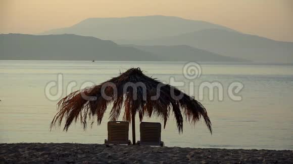 海滩上的躺椅和棕榈树伞在异国度假胜地放松度假带海和山的彩色日落视频的预览图