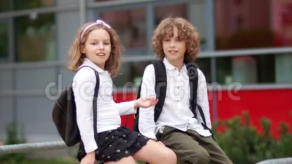 两个卷曲的学童学校的朋友愚蠢地坐在学校附近的栏杆上孩子们穿着视频的预览图