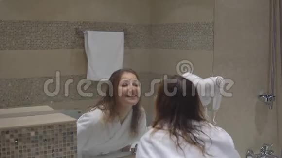 穿着白色长袍的滑稽迷人女孩在浴室的镜子前跳舞唱歌视频的预览图