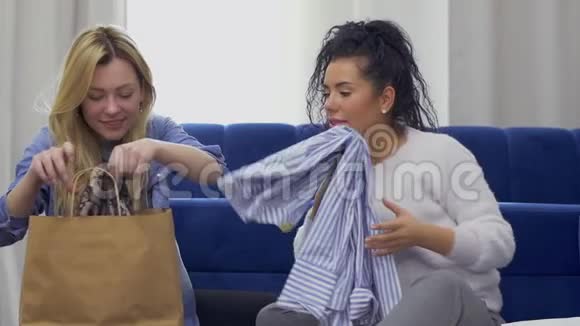 年轻的白种人金发女郎在购物后向她的朋友展示一件新买的衣服视频的预览图