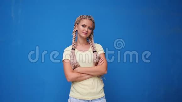 一位严肃的金发女孩女学生双臂交叉在蓝色背景上看镜头视频的预览图