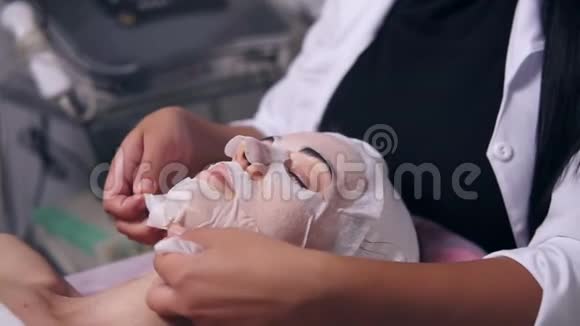 女性美容师正在从女性脸上摘下一个特殊面具用棉垫清洁她的脸专业人员视频的预览图