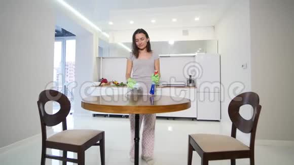 一个穿着紧身灰色T恤领口很深的女人用抹布擦拭一张大餐桌视频的预览图