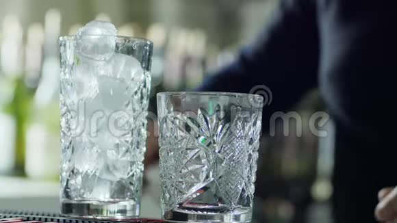 酒吧工作人员将金属勺举在手臂上将冰块桌上的透明玻璃特写中视频的预览图