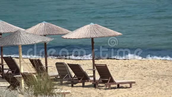 海浪带着草伞和木制日光浴床来到海滩的岸边视频的预览图