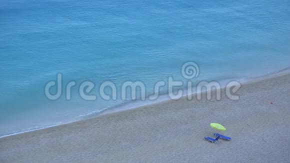 一把雨伞在靠近绿松石水的海滩上有两个日光浴床视频的预览图