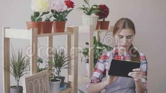 小生意一个穿着条纹围裙和格子衬衫的女孩站在一家花店里架子上有花和一朵视频的预览图