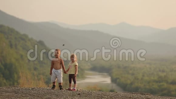 3岁至5岁的迷人的小孩在日落时站在山的边缘手牵手视频的预览图