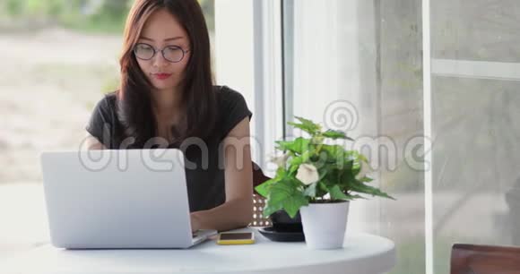 亚洲女人开始用她的笔记本电脑和手机工作视频的预览图