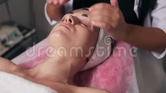 一位专业美容师的特写镜头他在水疗沙龙做面部和颈部按摩年轻女子躺在床上视频的预览图