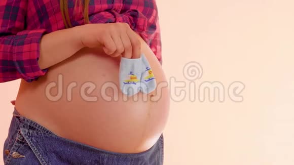 一个怀孕的女人在她赤裸的大肚子上带着可爱的新生袜子走路想让妈妈玩视频的预览图