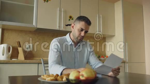 让年轻人阅读未付的账单并被妻子拥抱在家里的厨房里支持他视频的预览图