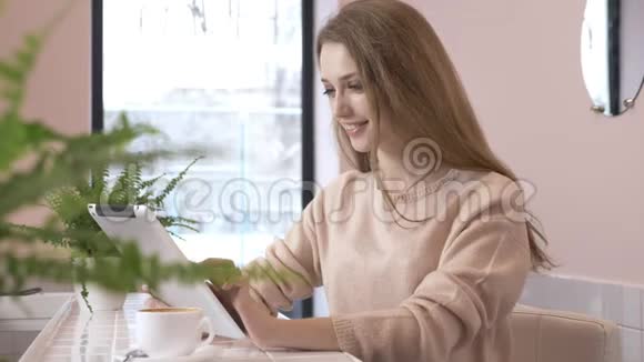 优雅美丽的白种人妇女使用平板电脑发短信打字在60英尺的咖啡馆里微笑视频的预览图