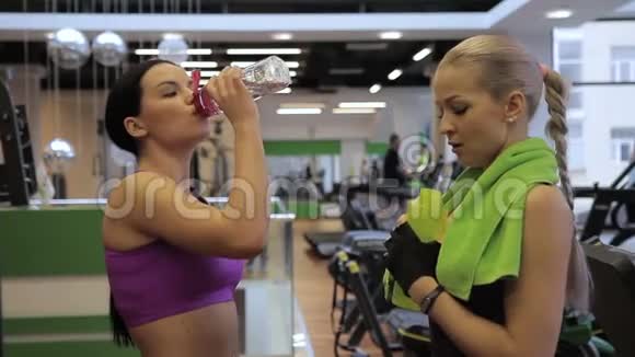 这两个年轻漂亮的女人站在现代的健身房和饮用水视频的预览图