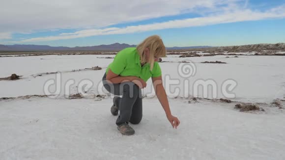 女人在沙漠中干燥的湖泊的白色水面上品尝盐视频的预览图