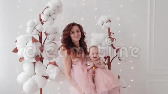 美丽的母亲和一个一岁的女儿在一个照相馆附近的人造棉花和发光墙视频的预览图