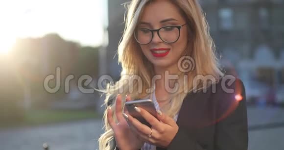 近距离观看一个活泼开朗的金发女商人她的红口红通过智能手机上网漂亮极了视频的预览图