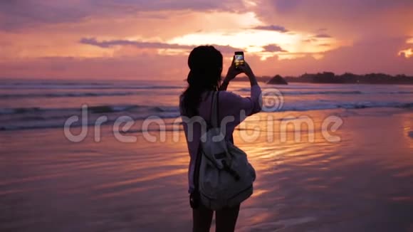 带背包的女孩在日落时拍一张海洋照片视频的预览图