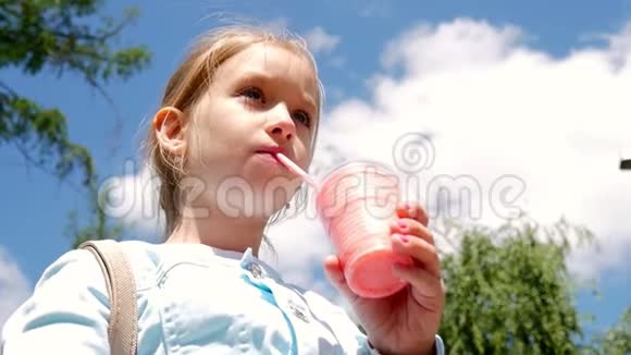可爱的小女孩正在用吸管喝鸡尾酒在阳光明媚的天气里站在公园里视频的预览图