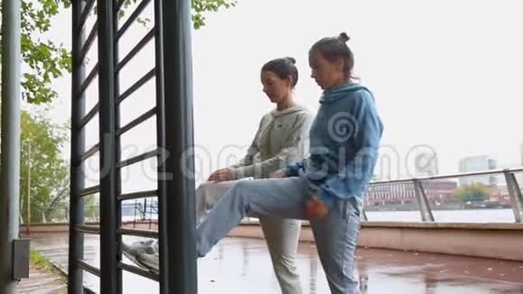 两个年轻漂亮的女孩双胞胎蹲在公园里做伸展运动减肥健身模特锻炼美丽的景色视频的预览图