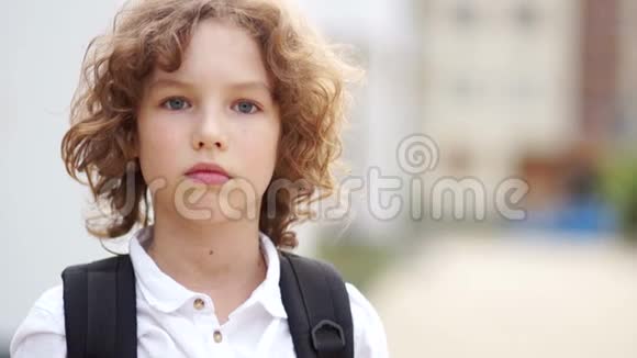 一个严肃的蓝眼睛留着卷发的小学生的肖像这个男孩既焦虑又悲伤回到学校视频的预览图