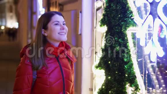 身穿红色外套的微笑女人站在装饰着圣诞树和花环的橱窗旁视频的预览图