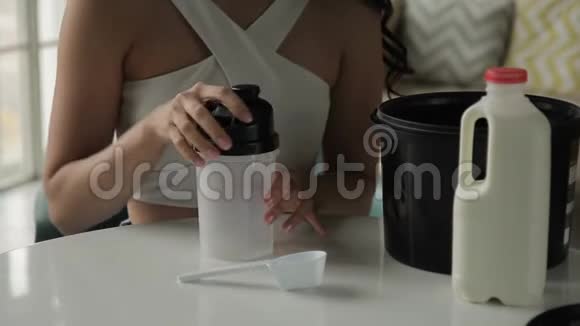 年轻女子坐在家里把蛋白质放进奶昔里视频的预览图
