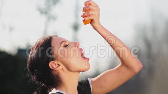 侧视特写迷人的年轻黑发将橙色和天然橙汁倒入她的嘴里视频的预览图