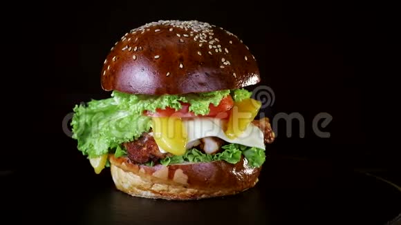 汉堡里有一大块肉青菜和奶酪正在黑色背景的木板上旋转视频的预览图