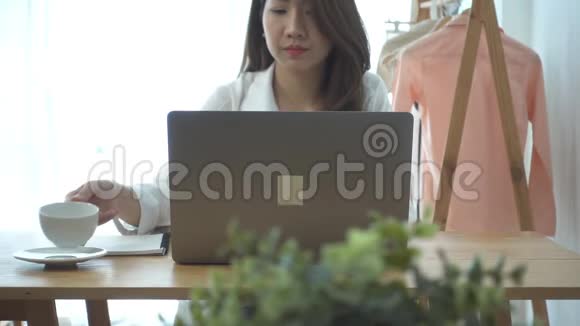 慢动作美丽的年轻微笑的女人工作在笔记本电脑同时享受喝温暖的咖啡坐在客厅在家里视频的预览图