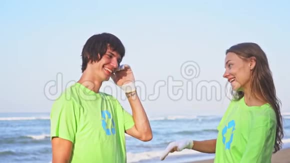 快乐的年轻志愿者穿着绿色t恤衫在海滩上进行图像回收向镜头致意视频的预览图