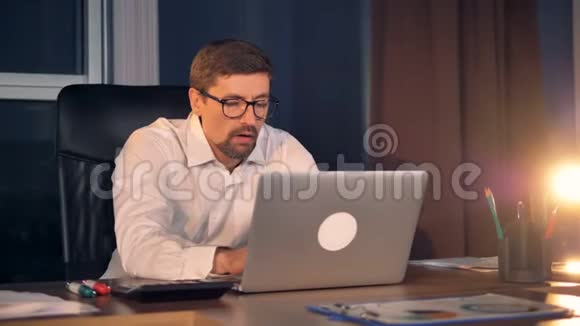 一个昏昏欲睡的商人在笔记本电脑上工作到很晚视频的预览图