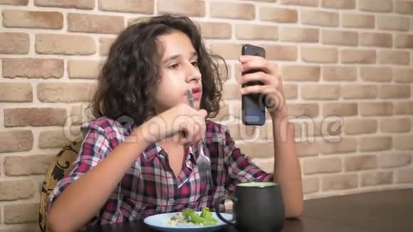 饥饿的少年在厨房里吃饭用智能手机视频的预览图