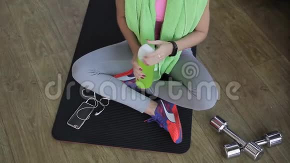 女运动员盘腿坐在健身房的黑色垫子上喝着瓶子里的水视频的预览图