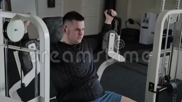 超重的成年男子在模拟器上训练他的胸部视频的预览图