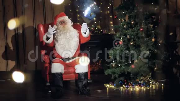 友好的圣诞老人用闪闪发光的手势在新年装饰的壁炉旁跳舞视频的预览图