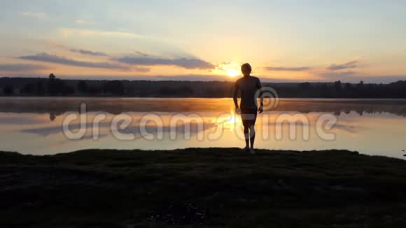 日落时分一个年轻人从湖边跑到一个摄影师那里视频的预览图