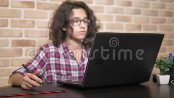 差不多了一个少年头发卷曲黑发穿着格子衬衫使用手写笔在一个图形平板上工作视频的预览图