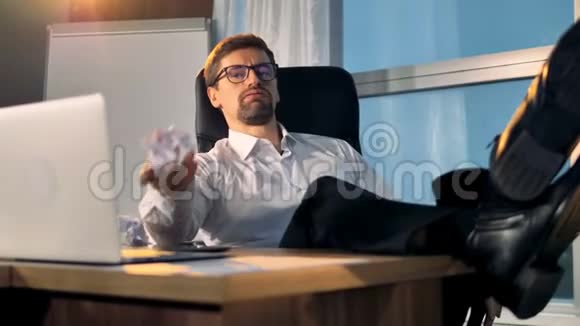 一个精疲力竭的商人坐在桌子上玩着皱巴巴的纸球4K视频的预览图