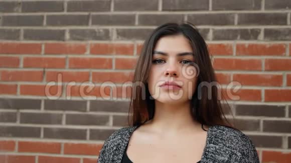 一个年轻自信的女人靠在砖墙上的肖像慢镜头视频的预览图