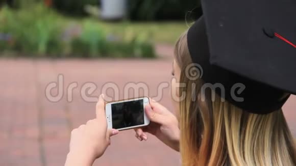 快乐的学生戴着毕业帽在智能手机上拍摄朋友假期视频的预览图