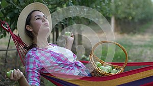 花园乡下的年轻女人拿着一篮子苹果躺在吊床上视频的预览图