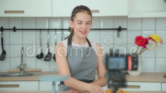 穿着灰色围裙的年轻女子带领一个烹饪博客拍摄视频视频的预览图
