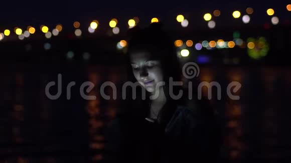 一个女孩很高兴站在一个夜晚城市的背景上使用智能手机视频的预览图