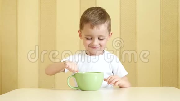 一个快乐的孩子坐在桌子旁用勺子从盘子里吃汤视频的预览图