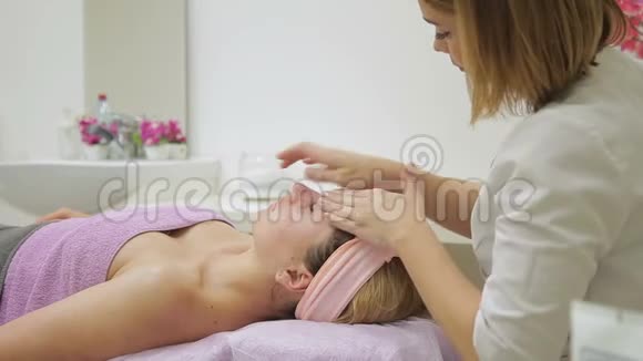 女性治疗师按摩水疗中心躺着的女士的脸视频的预览图