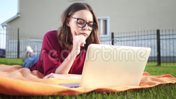 一个戴眼镜的女孩拿着笔记本电脑躺在后院视频的预览图
